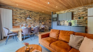 Een gezellige woonkamer met houten plafond, een bank, een salontafel en een eethoek met stoelen en een tafel.