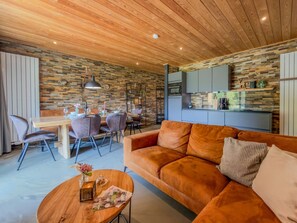 Ein gemütliches Wohnzimmer mit Holzbalkendecke, einer Couch, einem Couchtisch und einem Essbereich mit Stühlen und einem Tisch.