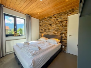Ein Schlafzimmer mit Bett, einem Fenster mit Blick und einer Holzbalkendecke.