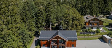 A modern lodge with a prominent wooden facade, a spacious patio area, and a view of a forested mountain backdrop.