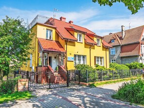 A yellow building with a red roof, a gated entrance, and a paved pathway. - Apartment Zenit by Interhome (Darlowo)