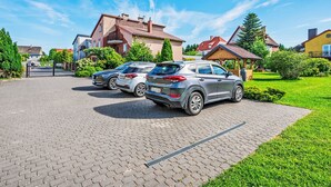 Ein gepflasterter Auffahrtsweg mit zwei parkenden Autos, ein Haus mit rotem Dach und einer gepflegten Rasenfläche.