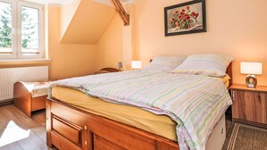 Ein Schlafzimmer mit schrägen Wänden, einem Bett mit gestreifter Bettwäsche, einem Nachttisch mit Lampe und einem Gemälde an der Wand.
