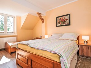 A bedroom with a sloped ceiling, a bed with striped bedding, a nightstand with a lamp, and a painting on the wall. - Apartment Zenit by Interhome (Darlowo)