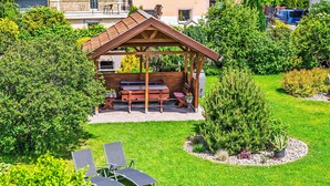 Ein Pavillon mit Grillplatz, umgeben von einem gepflegten Rasen und einem kleinen Baum.