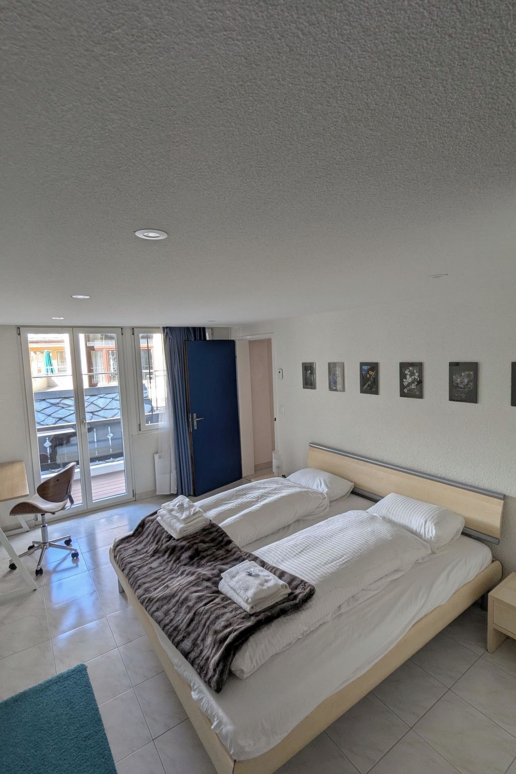 Une chambre d’hôtel avec un grand lit, un bureau et une chaise. Une porte donne accès à un balcon.