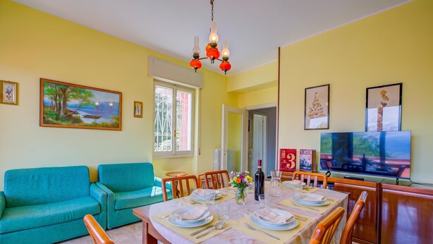 Un comedor con una mesa dispuesta para cuatro, un sofá y un televisor al fondo.