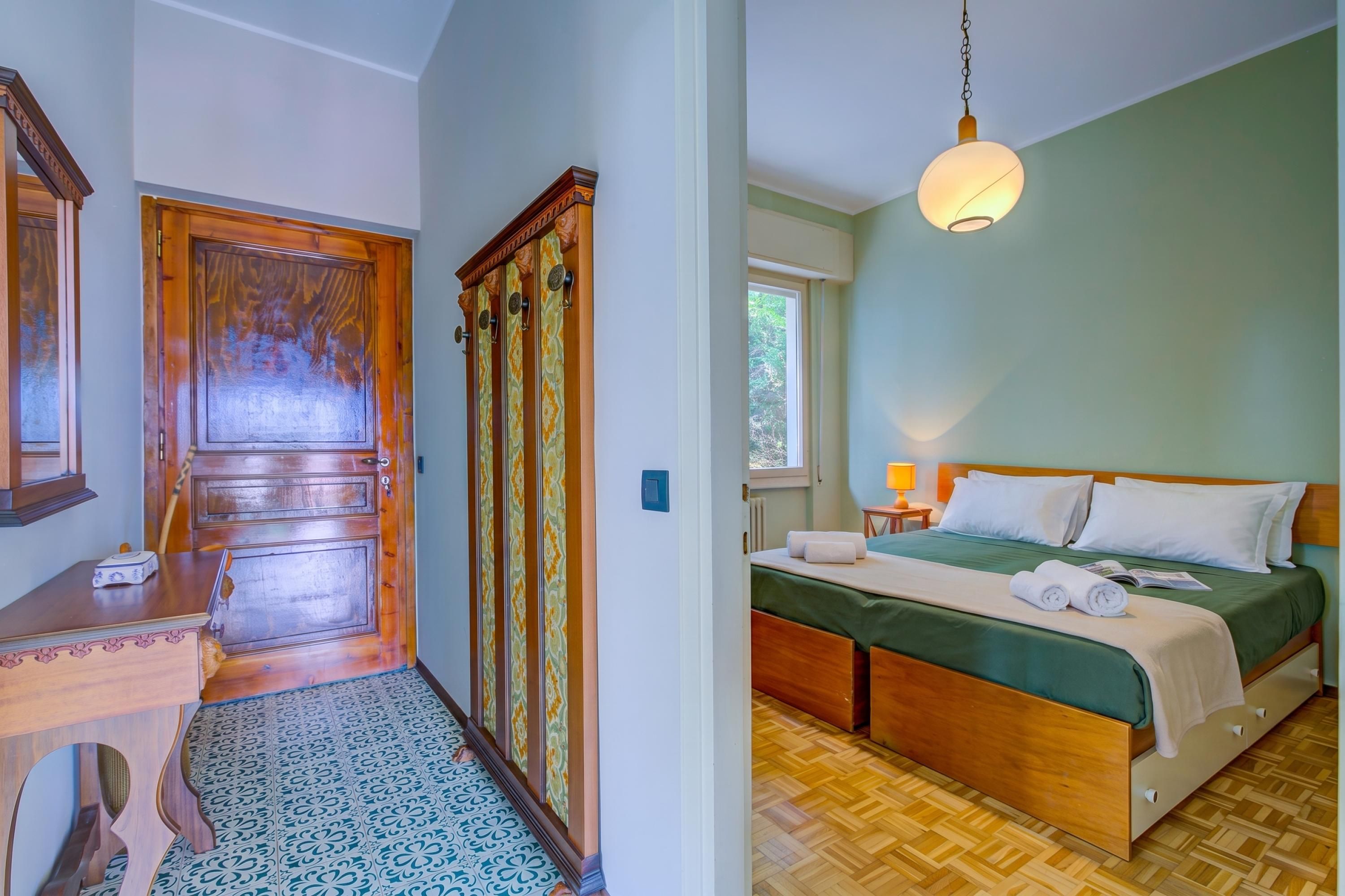 Una habitación con puerta de madera, una cama con cubrecama verde y una lámpara colgante.
