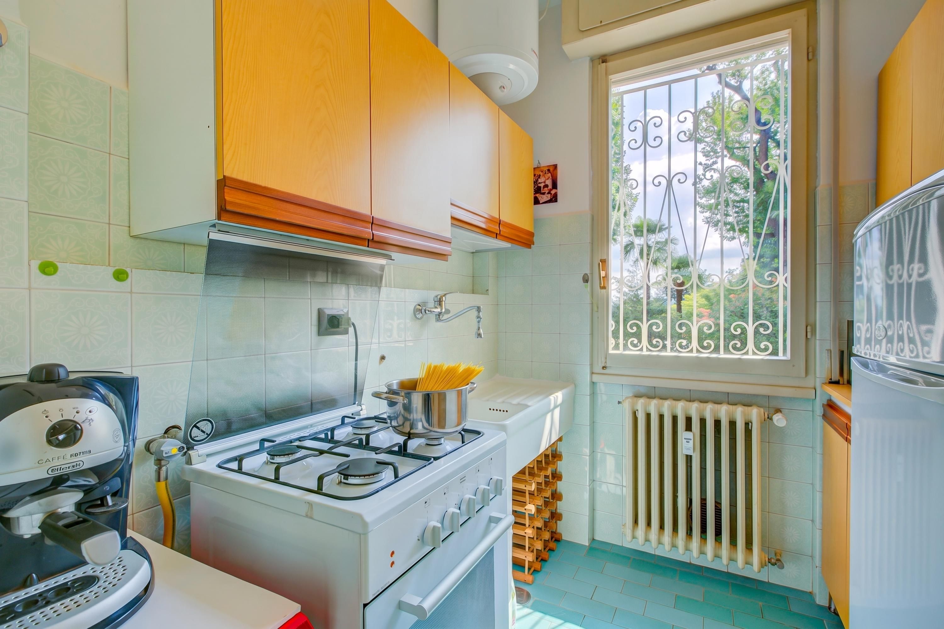 Cocina compacta con estufa a gas, cafetera y ventana con vistas a zonas verdes.