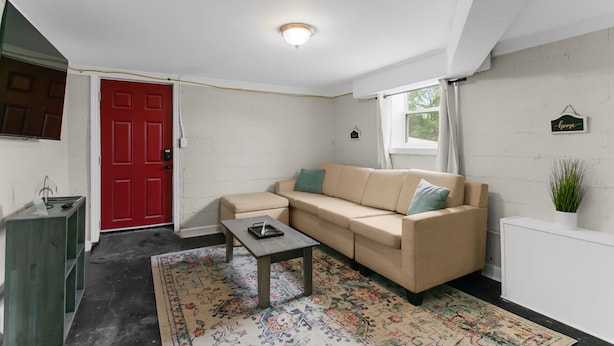 Un salón con sofá color beige, una mesita, una puerta roja y una pared blanca con un letrero que dice 'home'.