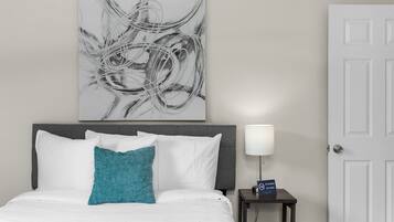Une chambre d’hôtel avec un lit, une table de chevet avec une lampe, un panneau « Il est interdit de fumer » et un tableau abstrait accroché au mur.