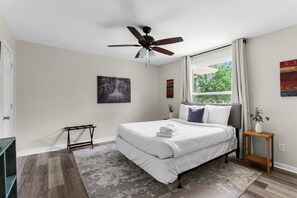 A bedroom with a bed, a ceiling fan, a window with curtains, and artwork on the walls.