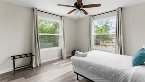 Une chambre à coucher avec un lit, un ventilateur de plafond et deux fenêtres avec des rideaux.