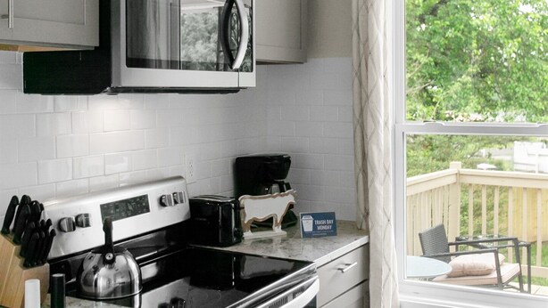 Une cuisine équipée d’un four à micro-ondes, d’une cuisinière et d’un grille-pain. Une fenêtre offre une vue sur la verdure environnante.