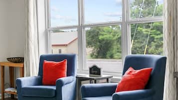 A room with two blue armchairs, a small table, and a view of the outdoors through large windows.