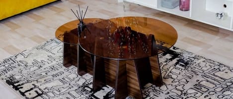 A round wooden coffee table with a glass top, surrounded by four legs, placed on a patterned rug.
