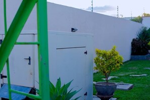 A white utility box with a small tree in a pot, a green metal structure, and a grassy area with a low wall. - Cosy 2bedroom apartment in mass media near east park mall - pet friendly (Lusaka)