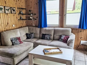 A living room with a sectional sofa, a coffee table, and a wall-mounted shelf with decorative items. - Vacation home Nina by Interhome (Extertal)