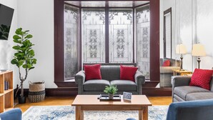 Un salon doté d’une baie vitrée, d’un canapé gris agrémenté de coussins rouges, d’une table basse en bois et d’une plante en pot.
