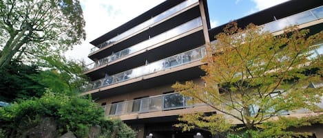 A multi-story building with a modern architectural design, featuring balconies and a landscaped entrance area.