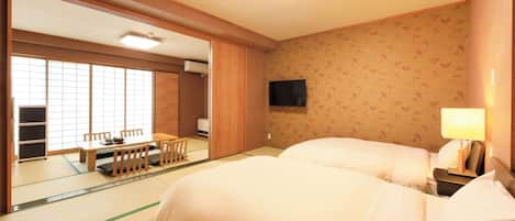 Una habitación japonesa tradicional con suelo de tatami, una cama futón, un televisor y una puerta corrediza que da a un comedor.