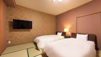Une chambre d’hôtel avec deux lits, un téléviseur à écran plat fixé au mur et une table de chevet avec une lampe.