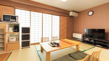 Une pièce de style japonais traditionnel, avec un sol recouvert de tatamis, une petite table basse sur laquelle est disposé un service à thé, un téléviseur et des portes coulissantes.