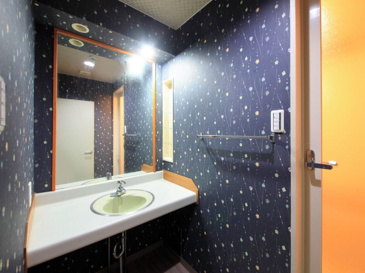 Ein Badezimmer mit einem weißen Waschbecken, einem Spiegel und einer Wand mit floralem Muster.
