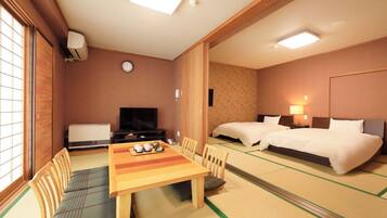 A hotel room with tatami flooring, a dining table with chairs, a television, two beds, and a small table with tea set.