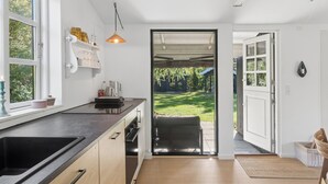 A modern kitchen with a large window, a pendant light, and a view of the garden through an open door. - Charming holiday home in beautiful Asserbo (Liseleje)