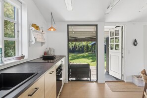 Eine moderne Küche mit einem großen Fenster, einer Pendelleuchte und Blick auf den Garten durch eine offene Tür.