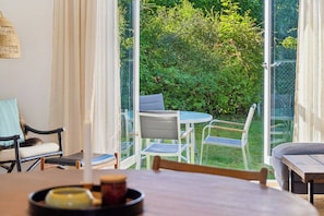 A room with a dining table, chairs, a sofa, and a view of a lush garden through glass doors. - Charming holiday home in beautiful Asserbo (Liseleje)
