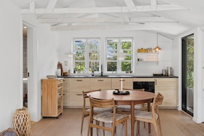 A modern kitchen with a dining area, featuring wooden cabinets, a round table, and a view through large windows. - Charming holiday home in beautiful Asserbo (Liseleje)