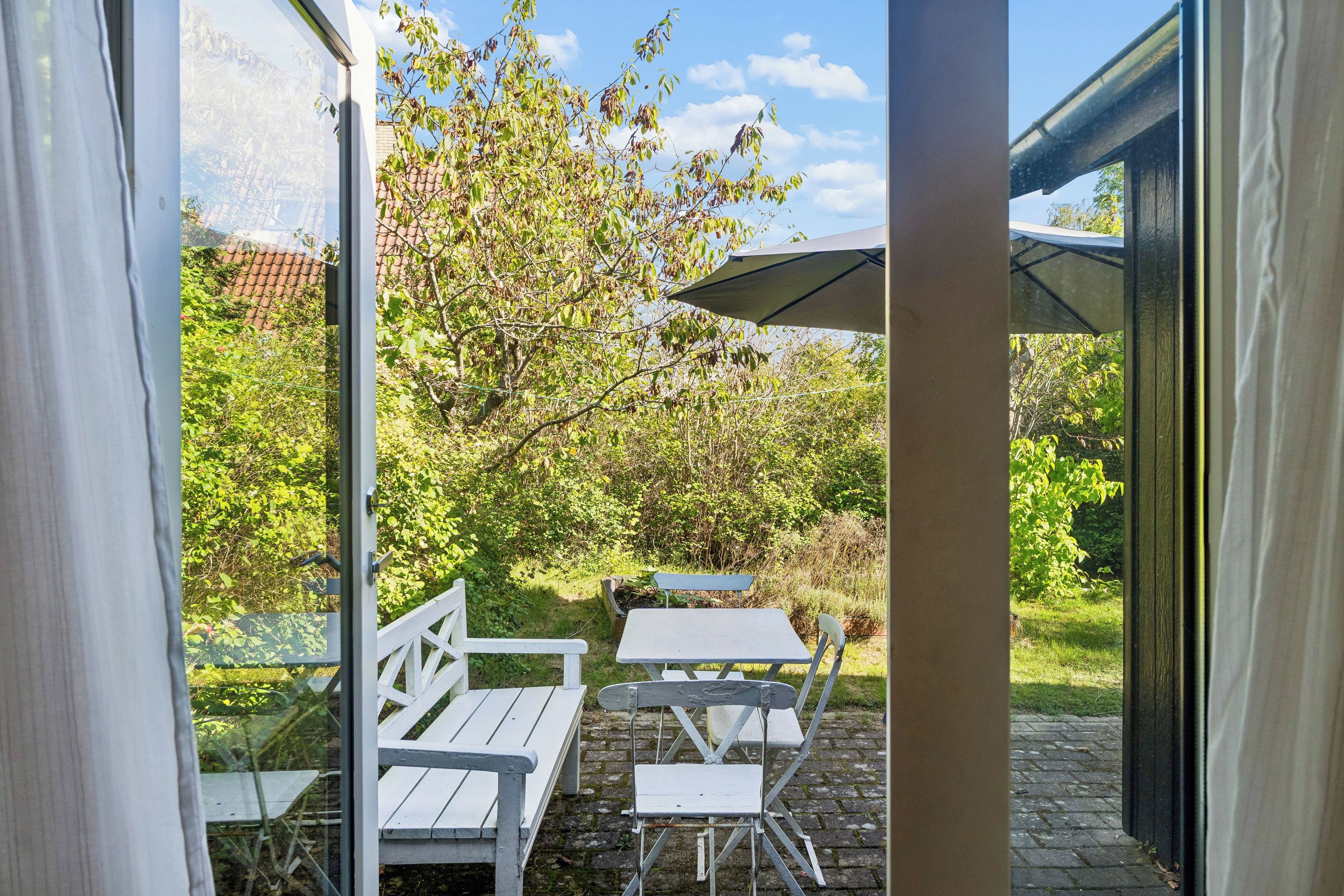 Een terras buiten met een tafel, stoelen, een bank en een grote parasol.