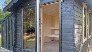 A log cabin with a sliding glass door leading to an interior with a wooden bench and a small table. - Charming holiday home in beautiful Asserbo (Liseleje)