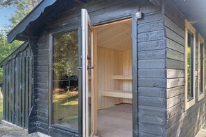 Eine Blockhütte mit einer Schiebetür, die zu einem Innenraum mit einer Holzbank und einem kleinen Tisch führt.