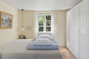 Ein Schlafzimmer mit Bett, Fenster, Gemälde und Bücherregal.