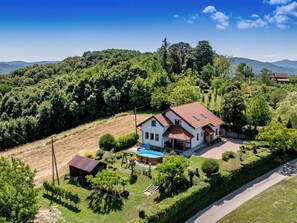 A two-story house with a red-tiled roof, surrounded by lush greenery and hills. - House Sofija by Interhome (Vrtlinovec)