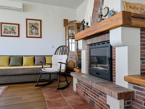 Ein Wohnzimmer mit Kamin, Schaukelstuhl, Sofa und zwei gerahmten Bildern an der Wand.