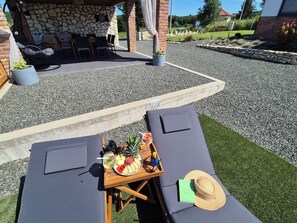 An outdoor seating area with a stone wall, a table with a fruit platter, and a hat on a lounge chair. - House Tilia Mellis by Interhome (Lužan Biškupečki)