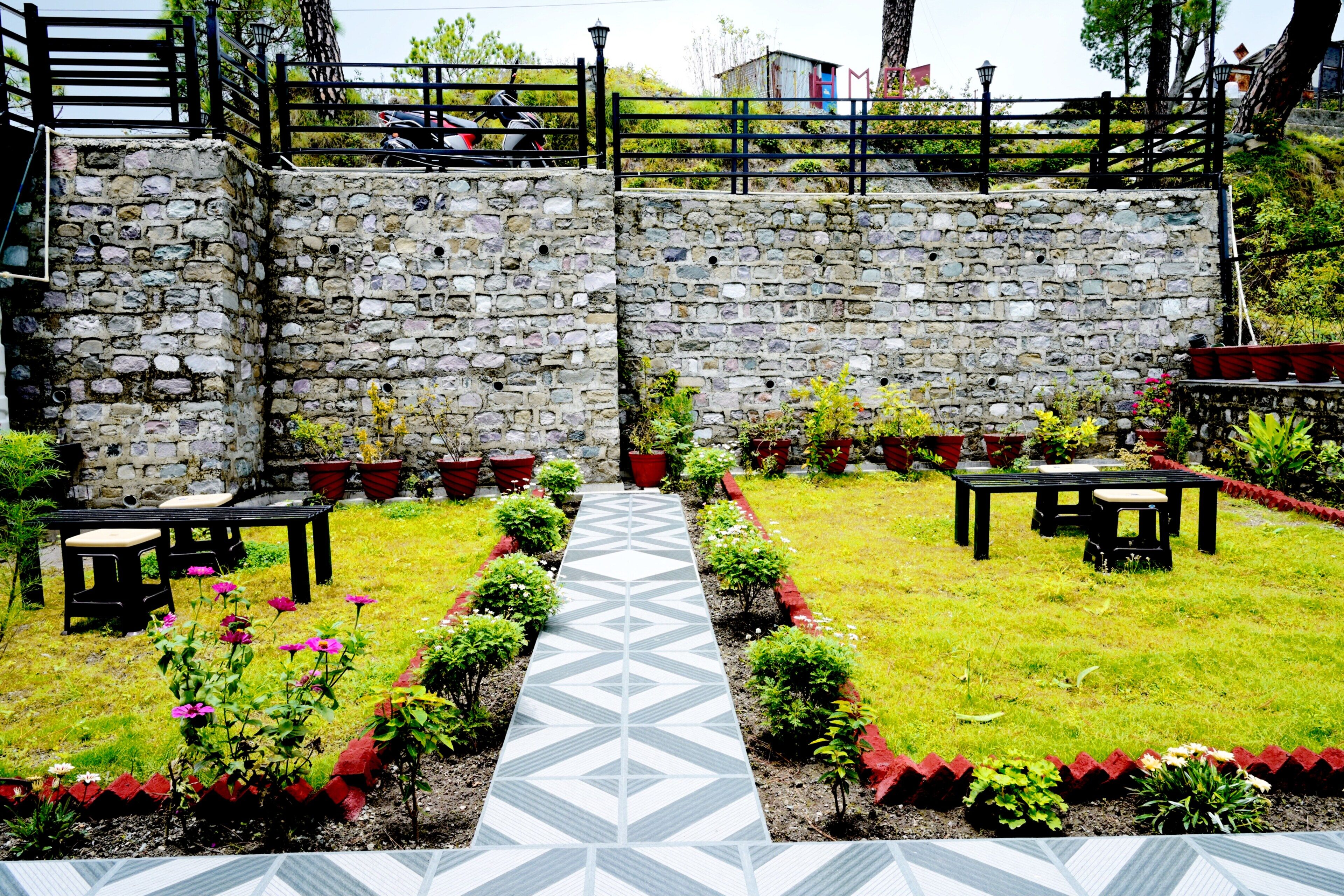 A stone wall with a paved walkway leading to a seating area with tables and chairs.