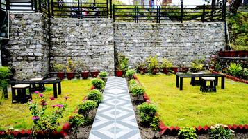 A stone wall with a paved walkway leading to a seating area with tables and chairs.