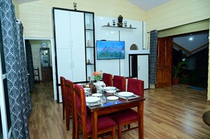 Comedor con mesa de madera dispuesta para cuatro personas, sillas tapizadas en rojo y un televisor montado en la pared.