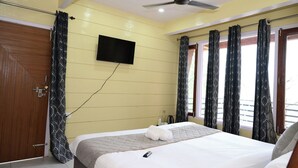 Hotelkamer met een bed, een aan de muur bevestigde televisie, een plafondventilator en een raam met gordijnen.