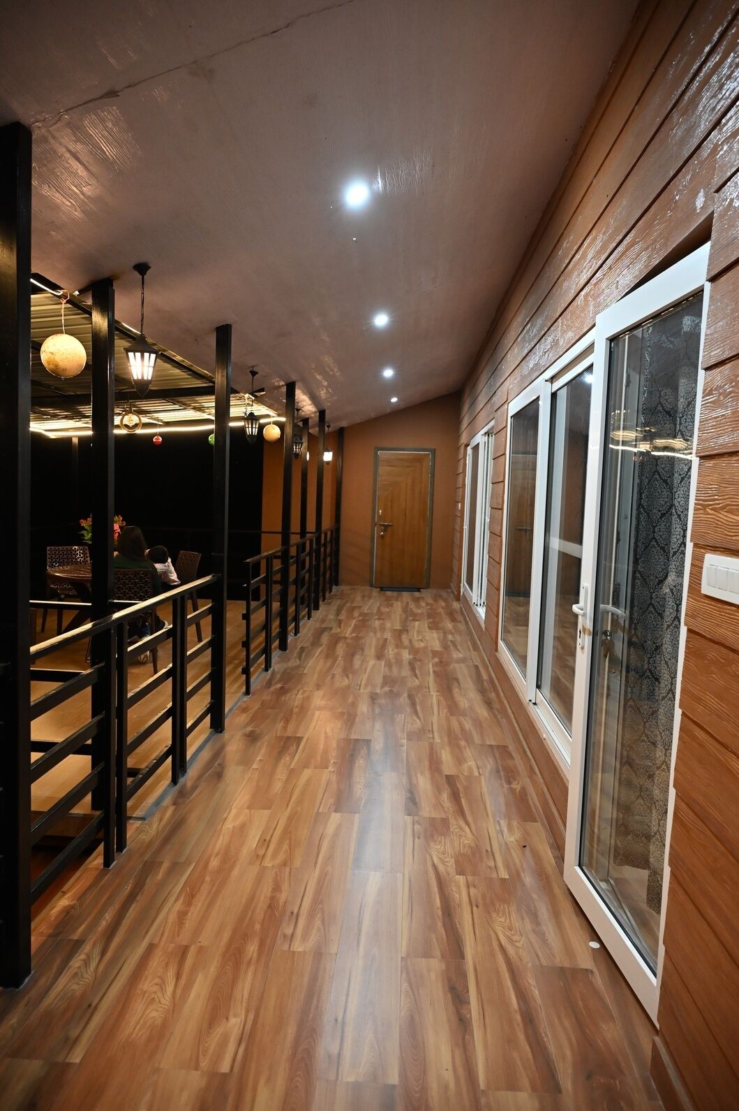 A corridor with wooden flooring, a metal railing, and a door at the end.
