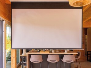 A room with a large white projection screen, three chairs, and a wooden table with various items. - House Dobra vila by Interhome (Zadobarje)