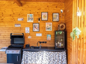 Een houten hut van binnen, met een grill, een gootsteen en een kast met flessen.