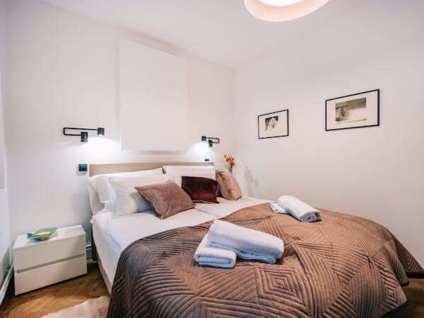 A neatly arranged hotel room with a bed, bedside tables, and wall-mounted lights.