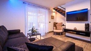 Un soggiorno moderno con un divano, un tavolino, una TV a parete e una scala che conduce a un livello superiore.