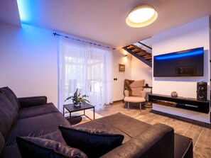 Ein modernes Wohnzimmer mit einer Couch, einem Couchtisch, einem an der Wand befestigten Fernseher und einer Treppe, die zu einer oberen Ebene führt.